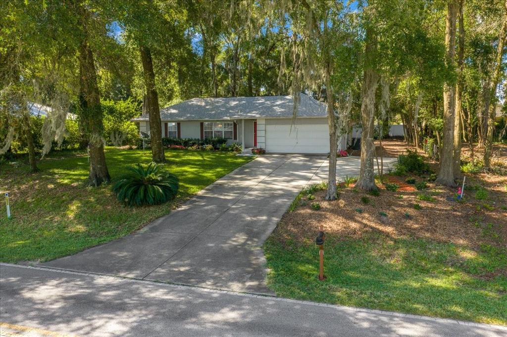 A single-story house with a white garage and driveway sits among trees in a yard — 3100 NE 35TH STREET, OCALA, FL