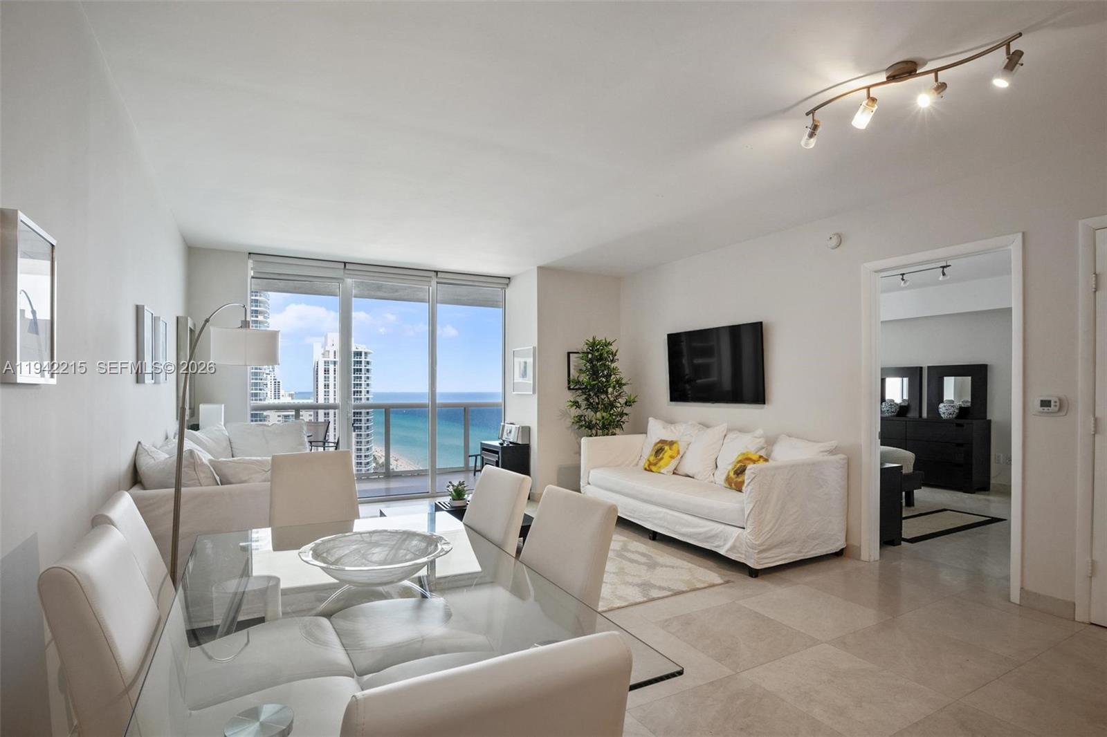 A bright living and dining area features white furniture, tile floors, and ocean views — 1830 S OCEAN DR # 2110, Hallandale Beach FL 33009, HALLANDALE BEACH, FL