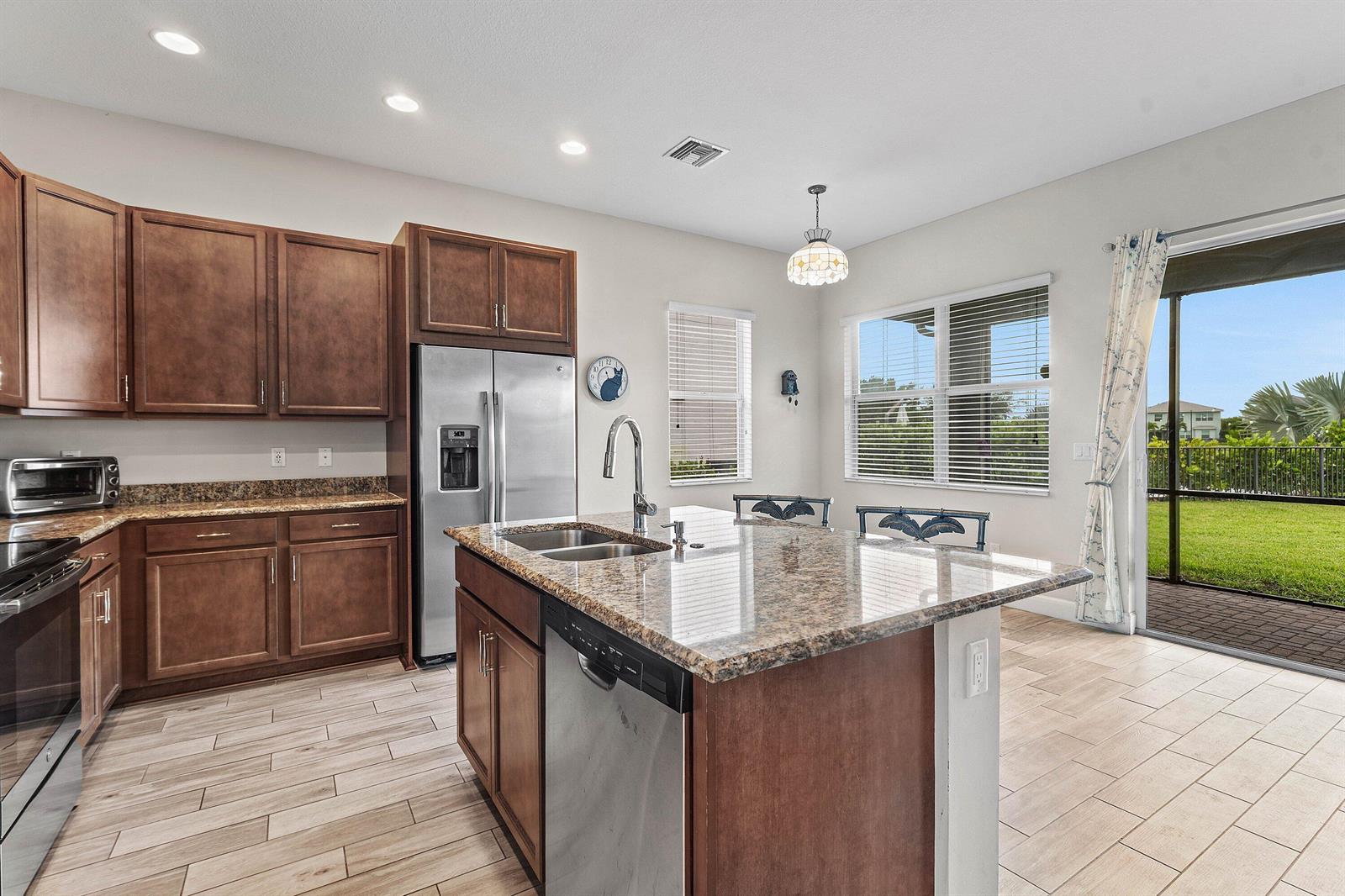 A kitchen features brown cabinets, granite countertops, a center island, and a sliding glass door — 5921 Switchgrass Lane, FL 33470, FL