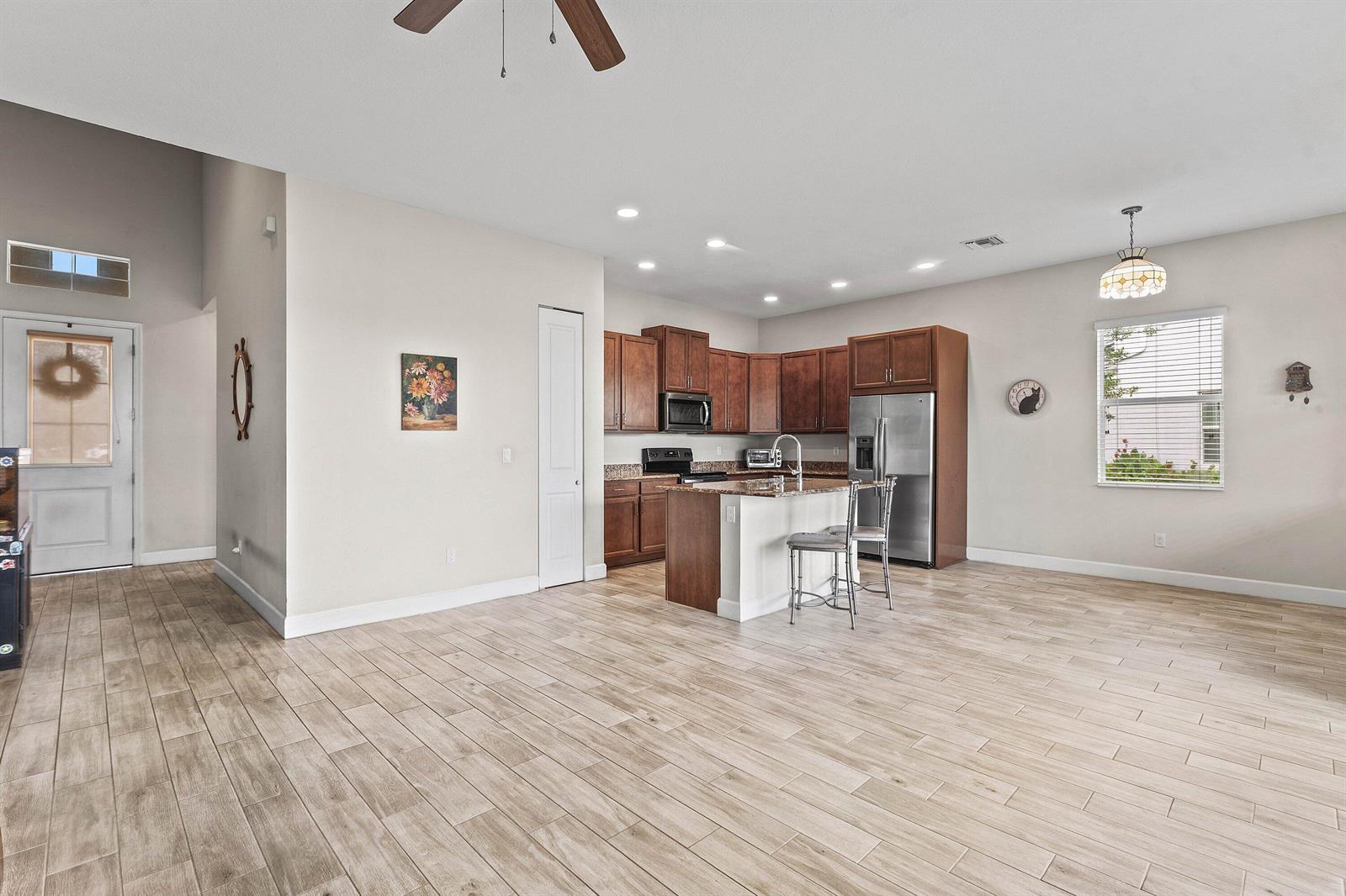 An open-concept kitchen features dark wood cabinets, a granite island, and light wood-look flooring — 5921 Switchgrass Lane, FL 33470, FL