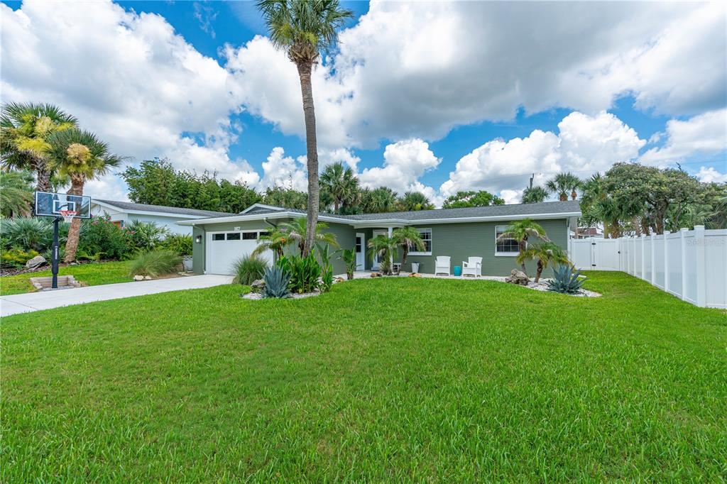 A single-story green house with a white garage door, palm trees, and a front lawn — 167 ROYAL DUNES BOULEVARD, ORMOND BEACH, FL