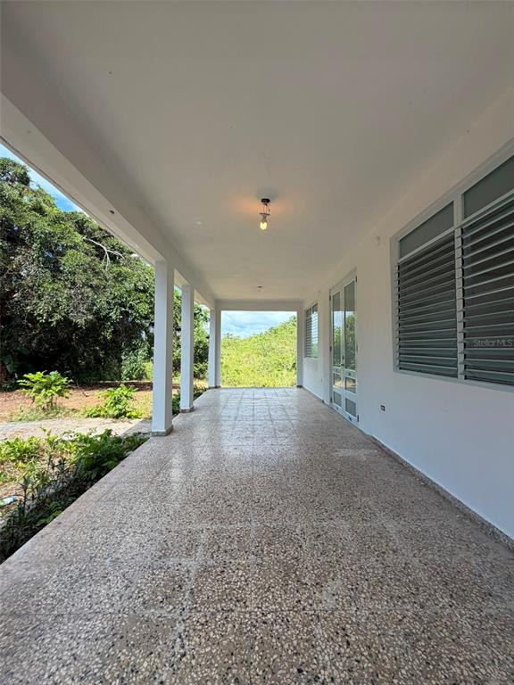 A covered outdoor patio features a speckled tile floor, white columns, and louvered windows — Ranchos Nativos ORQUIDEA ST LOT 43, VEGA ALTA, PR