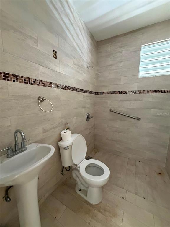 A bathroom features a pedestal sink, a toilet, and tiled walls with a decorative border — Ranchos Nativos ORQUIDEA ST LOT 43, VEGA ALTA, PR