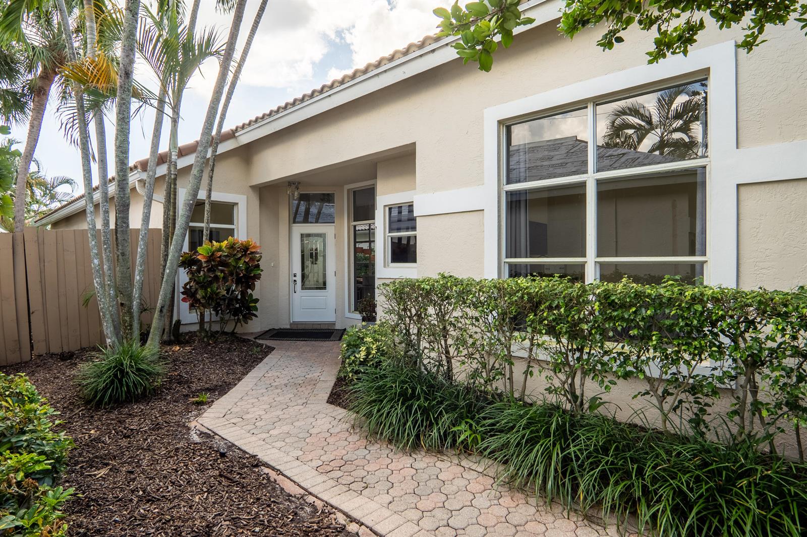 A paved walkway leads to the front entrance of a beige house with palm trees — 6670 NW 27th Avenue, Boca Raton FL 33496, BOCA RATON, FL