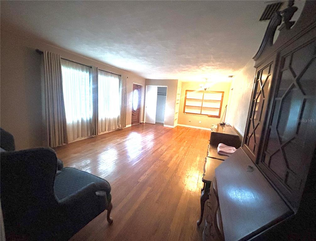 A spacious living room features hardwood floors, large windows with curtains, and a wooden hutch — 347 S 2ND STREET, EAGLE LAKE, FL