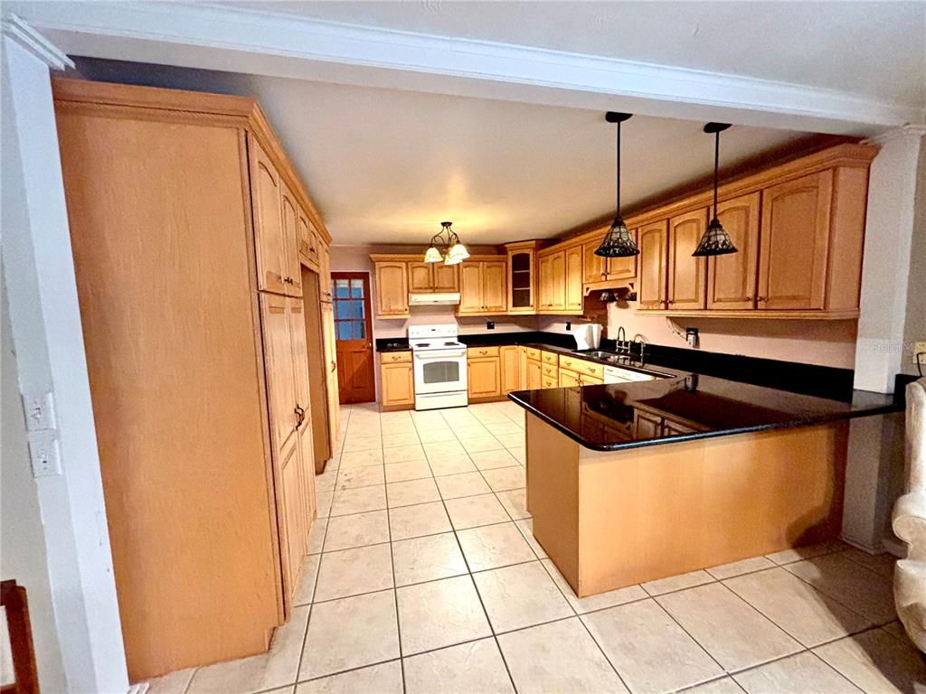 A kitchen features light wood cabinets, black countertops, tile flooring, and a central island — 347 S 2ND STREET, EAGLE LAKE, FL