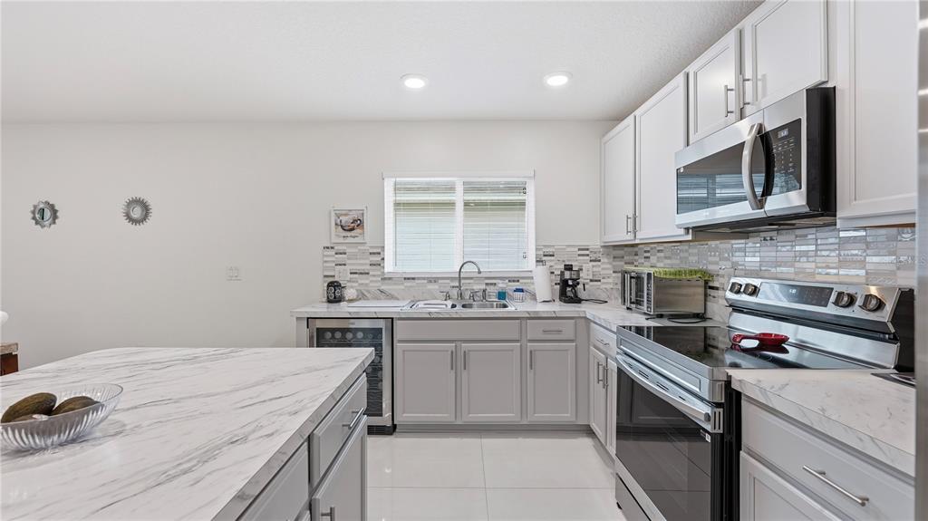 A modern kitchen features gray cabinets, white marble-look countertops, stainless steel appliances, and tile backsplash — 2457 BULRUSH DRIVE, ST CLOUD, FL
