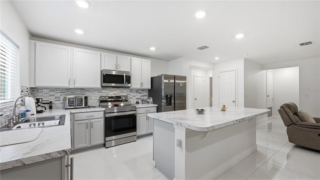 A modern kitchen features white cabinetry, stainless steel appliances, and a marble-patterned island countertop — 2457 BULRUSH DRIVE, ST CLOUD, FL