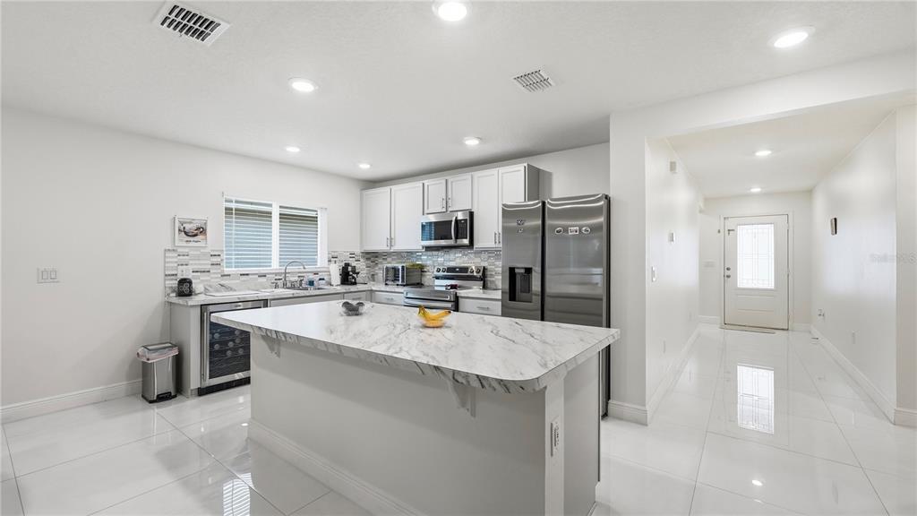 A modern kitchen features white cabinets, a marble-topped island, stainless steel appliances, and tile flooring — 2457 BULRUSH DRIVE, ST CLOUD, FL
