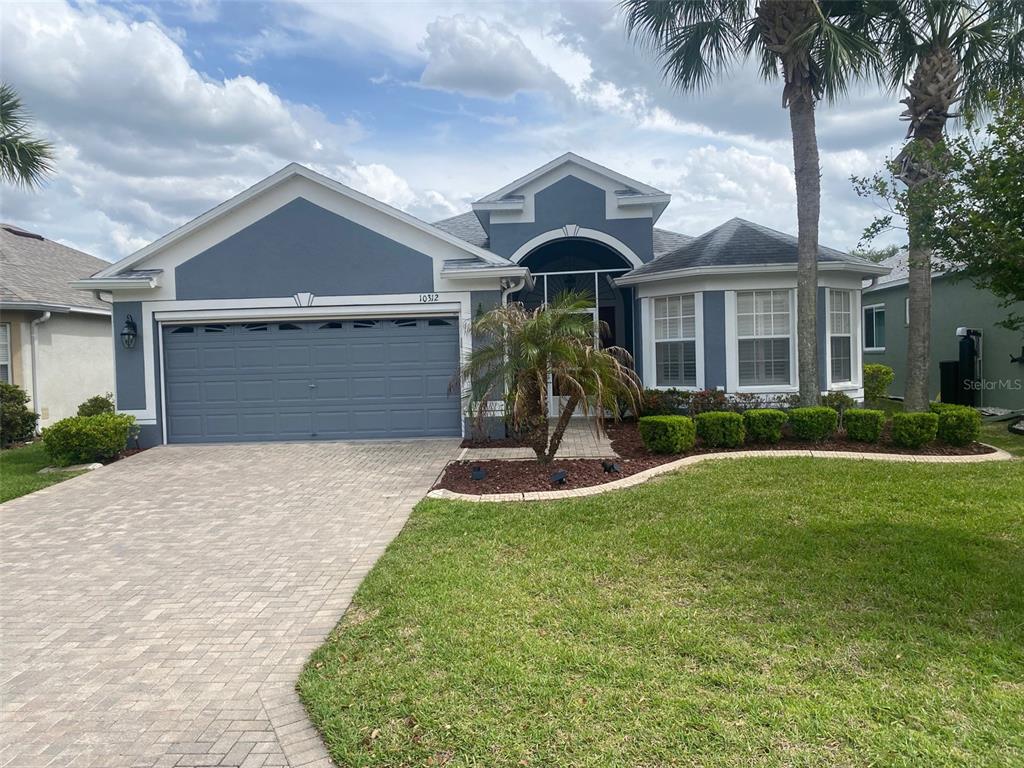 A blue single-story house features a two-car garage, a paved driveway, and a landscaped yard — 10312 OLD TAMPA BAY DRIVE, SAN ANTONIO, FL