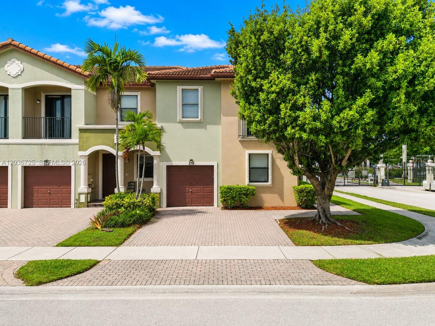 A two-story townhouse with a paved driveway, a garage, and a large tree in front — 678 NE 33rd Ter, Homestead FL 33033, HOMESTEAD, FL