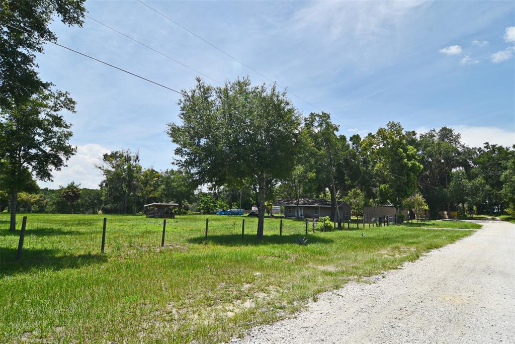 A gravel road runs alongside a fenced grassy lot with trees and a small house — 3100 POVERTY LANE, APOPKA, FL