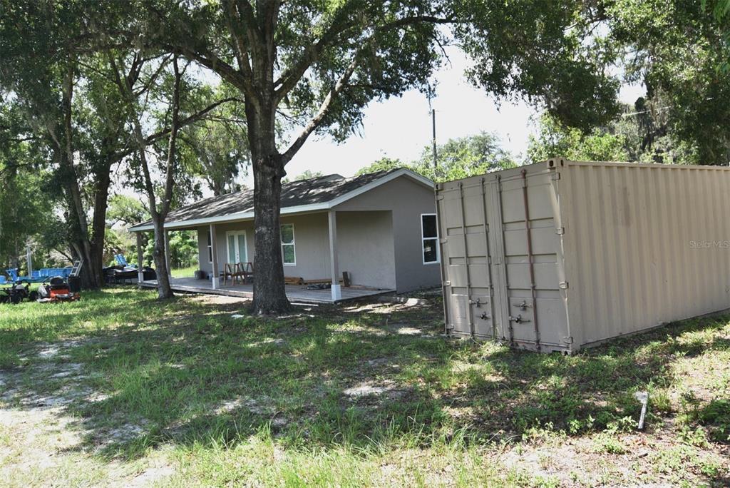 A tan shipping container sits in the yard next to a small house with a porch — 3100 POVERTY LANE, APOPKA, FL