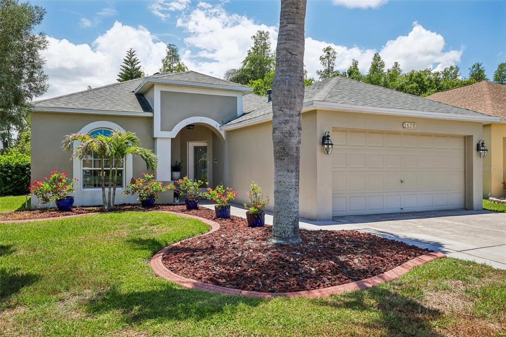 A single-story house with a beige stucco exterior, a two-car garage, and a landscaped yard — 1628 CROSSVINE COURT, TRINITY, FL