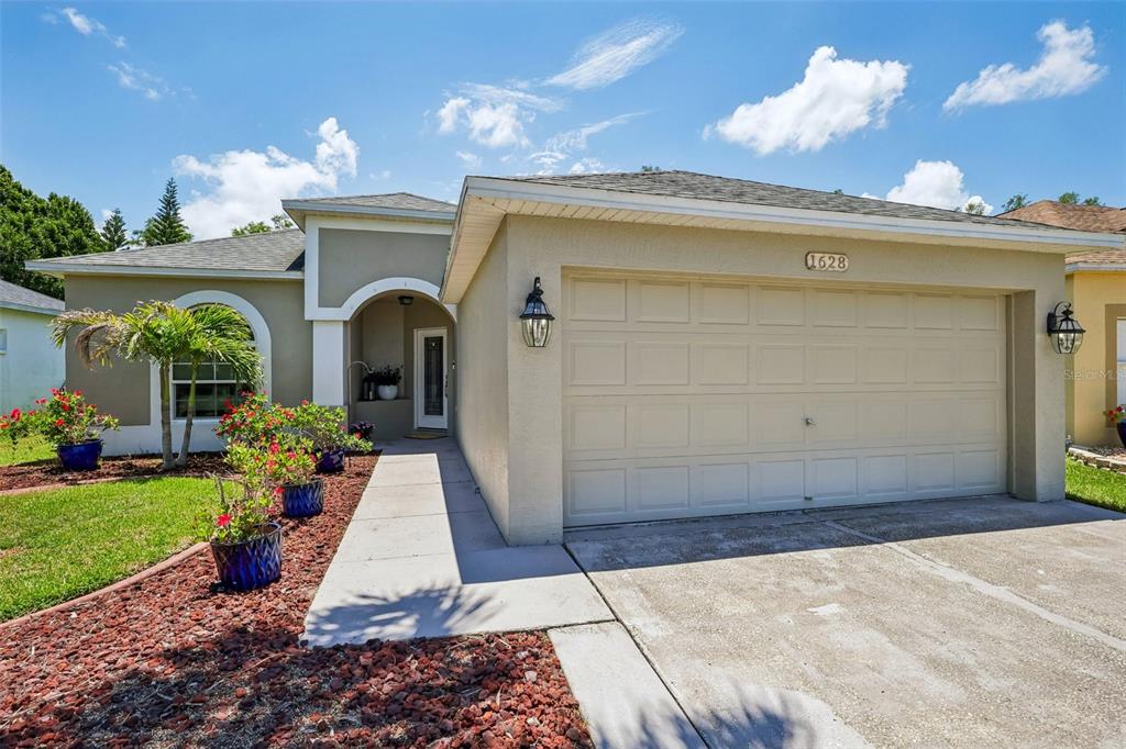 A single-story house with a beige stucco exterior, a two-car garage, and a landscaped yard — 1628 CROSSVINE COURT, TRINITY, FL