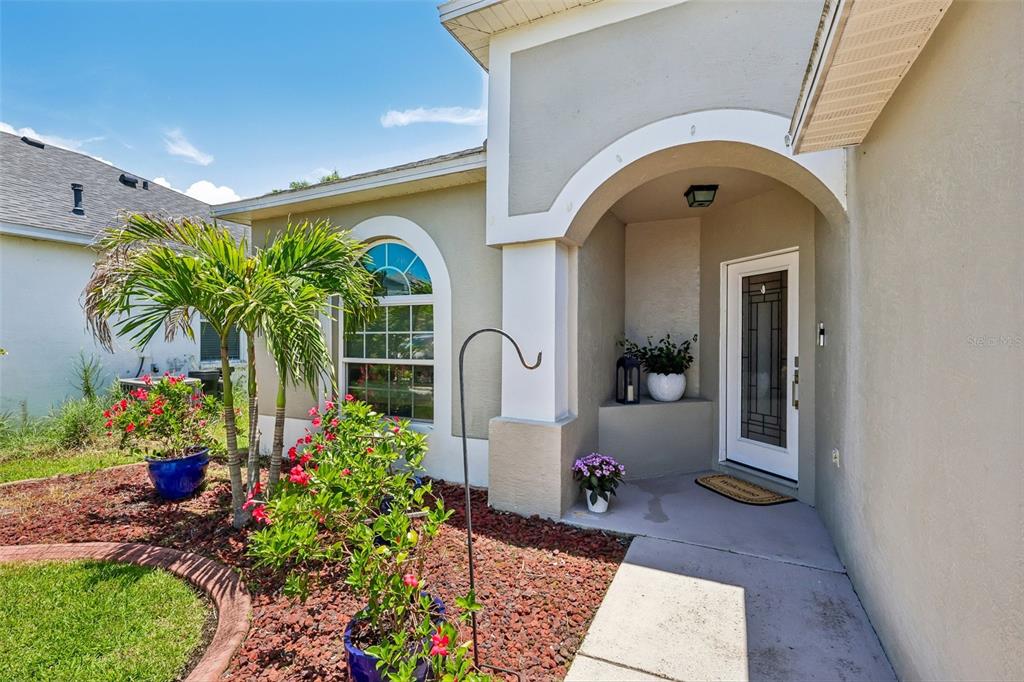 The exterior of a house features a covered entryway, a front door, and landscaped garden beds — 1628 CROSSVINE COURT, TRINITY, FL