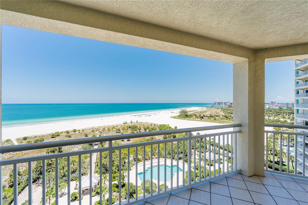 A balcony with a tiled floor overlooks a sandy beach, the ocean, and a pool — 1180 GULF BOULEVARD UNIT 1202, CLEARWATER BEACH, FL