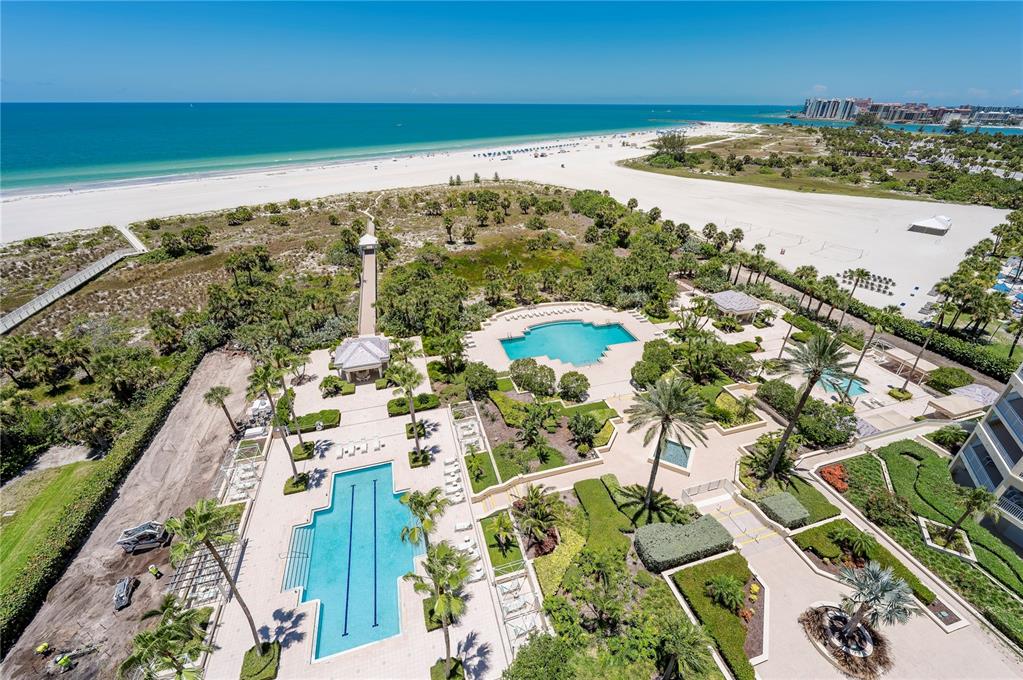 An aerial view shows a beach resort with two swimming pools, landscaped gardens, and walkways — 1180 GULF BOULEVARD UNIT 1202, CLEARWATER BEACH, FL
