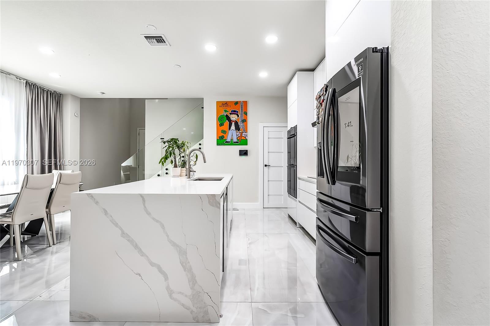 A modern kitchen features a marble waterfall island, white cabinetry, and a black refrigerator — 4566 Ficus St, Hollywood FL 33021, HOLLYWOOD, FL