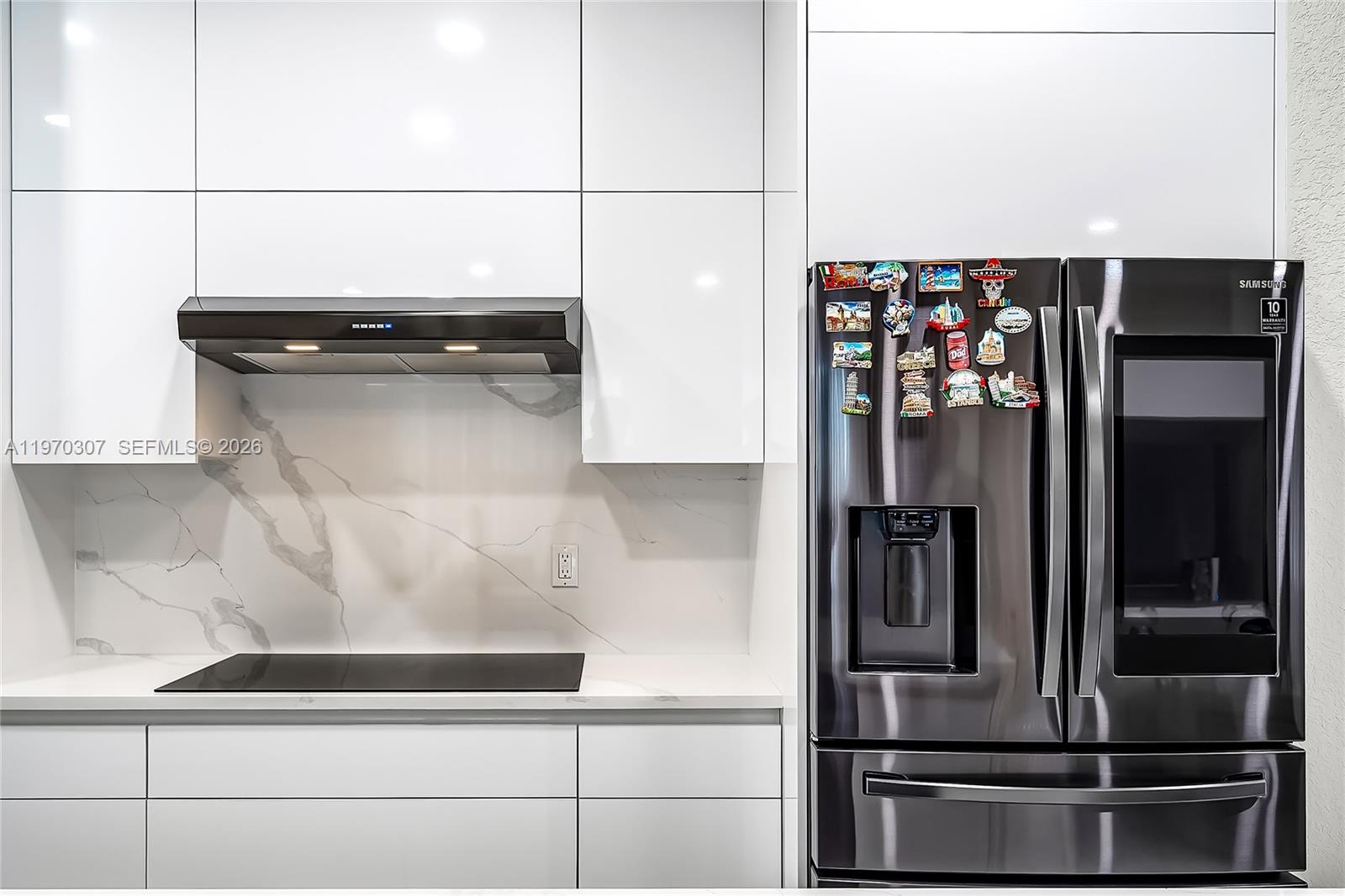 A modern kitchen features white cabinets, a marble backsplash, a black cooktop, and a refrigerator — 4566 Ficus St, Hollywood FL 33021, HOLLYWOOD, FL