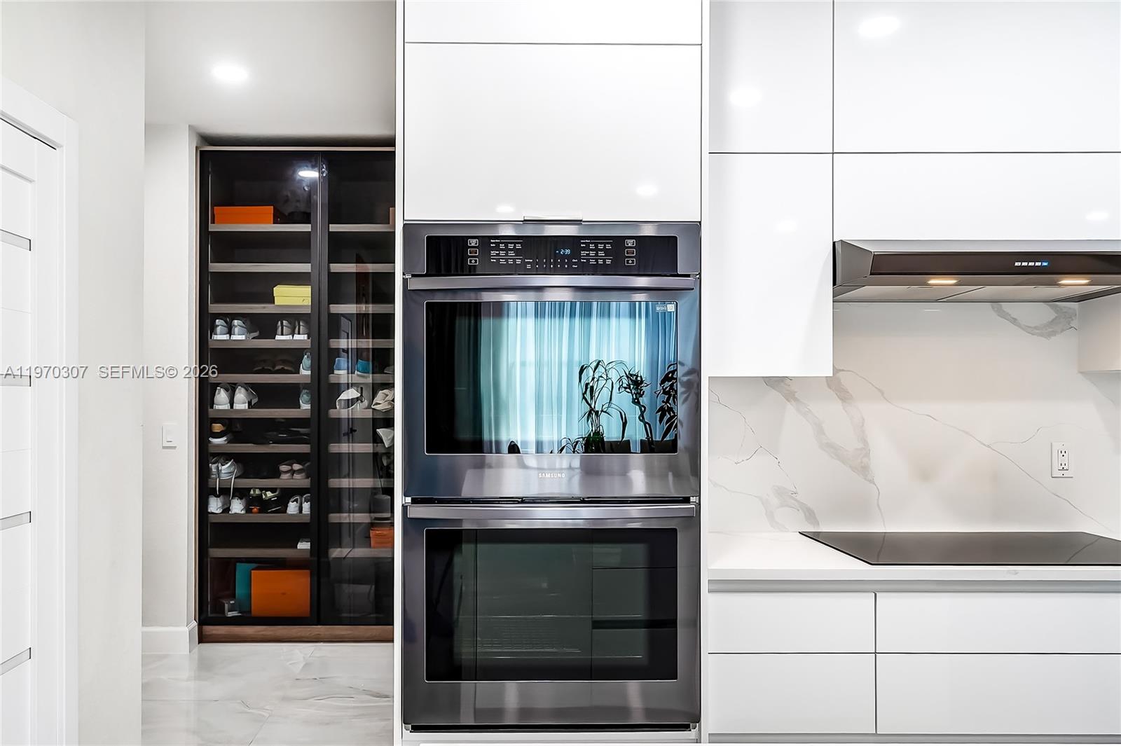 A modern kitchen features white cabinetry, a double wall oven, and a glass-enclosed shoe display — 4566 Ficus St, Hollywood FL 33021, HOLLYWOOD, FL