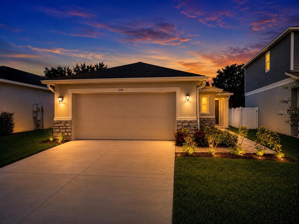 A single-story house with a two-car garage and stone accents at sunset — 1084 PAPAYA CIRCLE, DAVENPORT, FL
