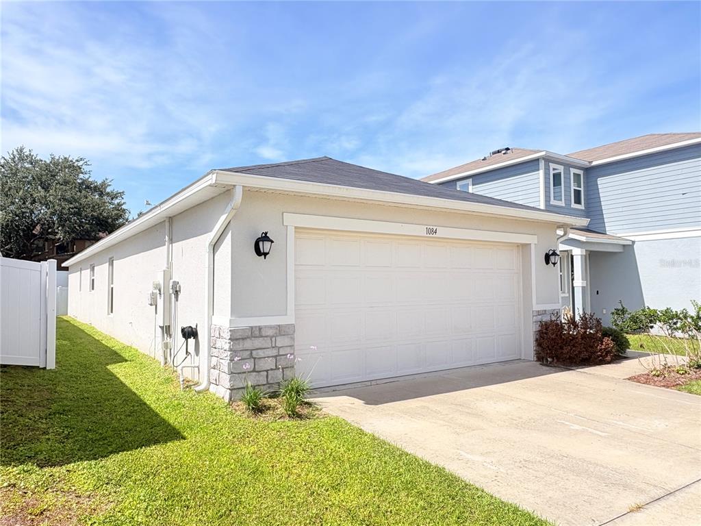 A light-colored house exterior features a two-car garage, stone accents, and a concrete driveway — 1084 PAPAYA CIRCLE, DAVENPORT, FL