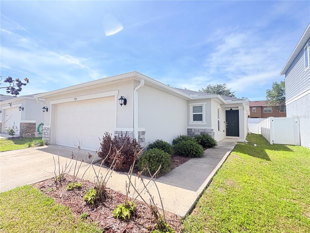 A single-story house with a white garage, stone accents, and a black front door — 1084 PAPAYA CIRCLE, DAVENPORT, FL