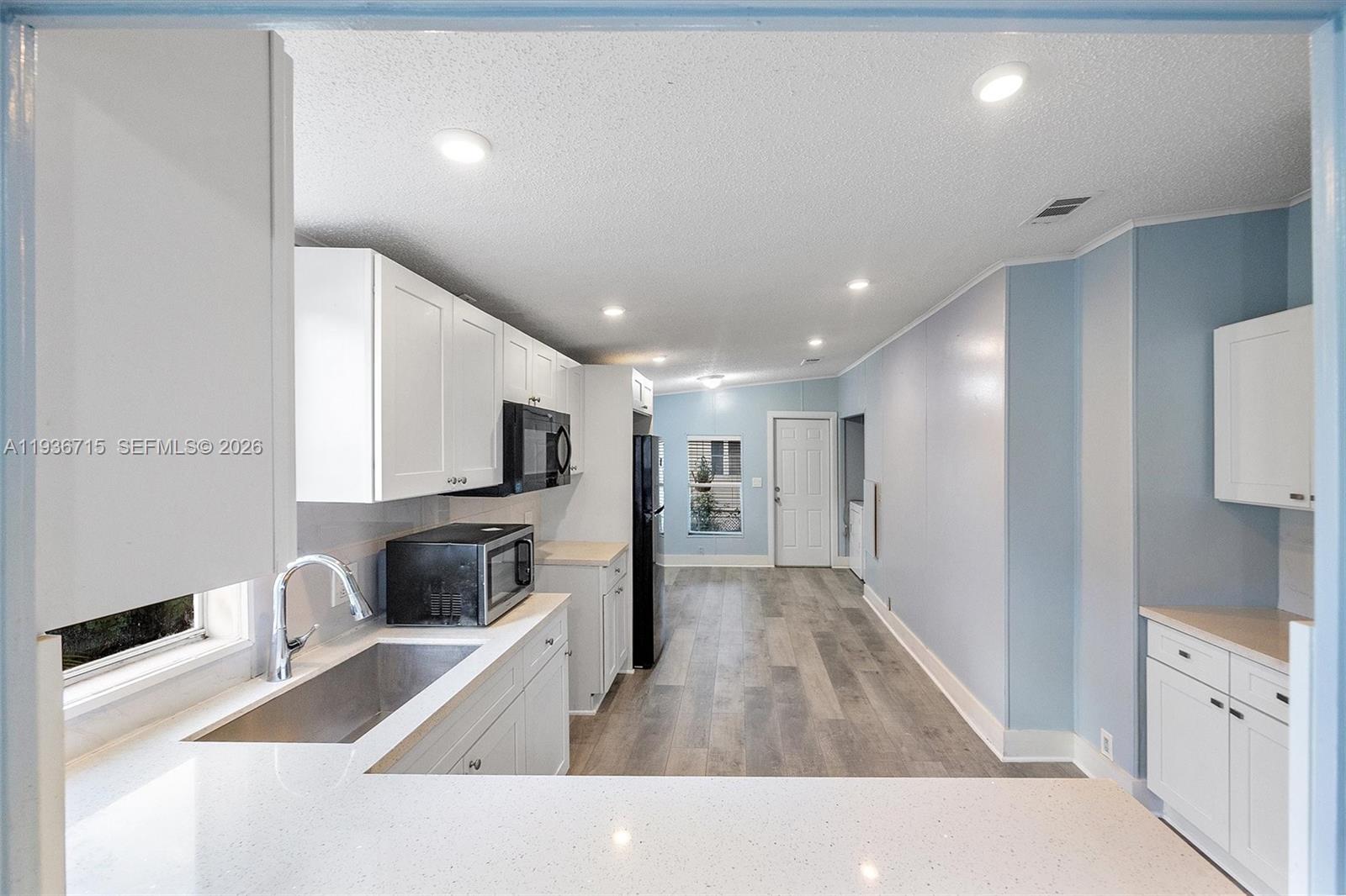 A kitchen with white cabinets, light countertops, and wood-look flooring leads to a doorway — 19800 SW 180th Ave Lot 222, Miami FL 33187, MIAMI, FL