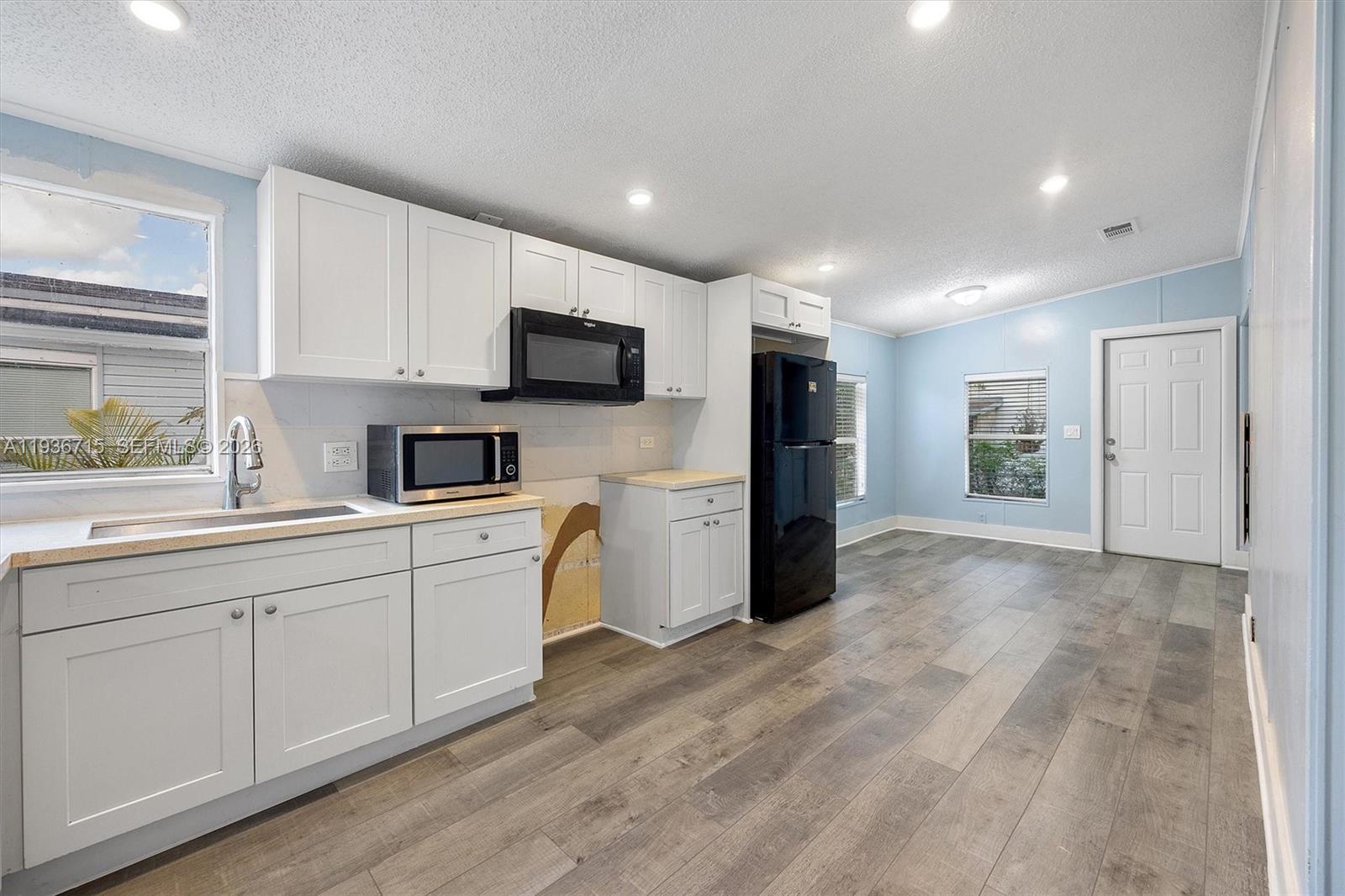 A kitchen with white cabinets, black appliances, light blue walls, and wood-look flooring — 19800 SW 180th Ave Lot 222, Miami FL 33187, MIAMI, FL