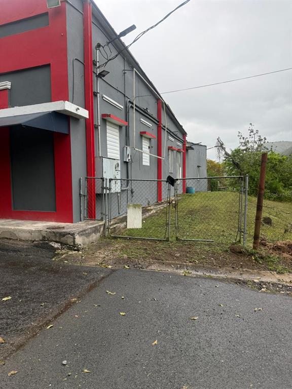 A gray and red building exterior with a chain-link fence and a grassy yard — PR 14 BARRIO MATON, CAYEY, PR