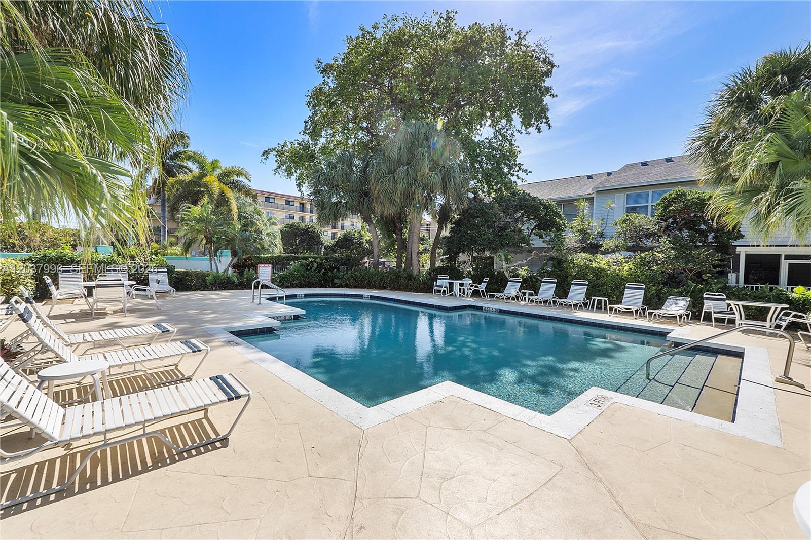 An outdoor swimming pool is surrounded by lounge chairs, palm trees, and lush landscaping — POMPANO BEACH, FL