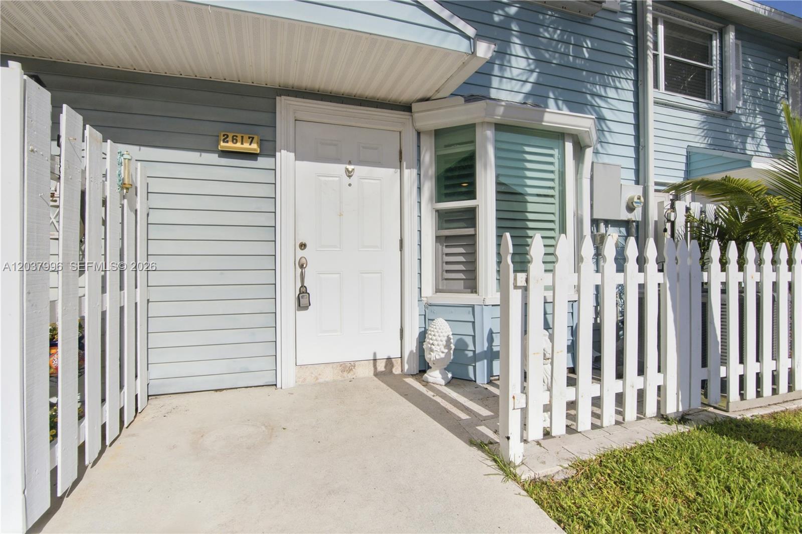 The exterior of a light blue house features a white front door and picket fence — POMPANO BEACH, FL
