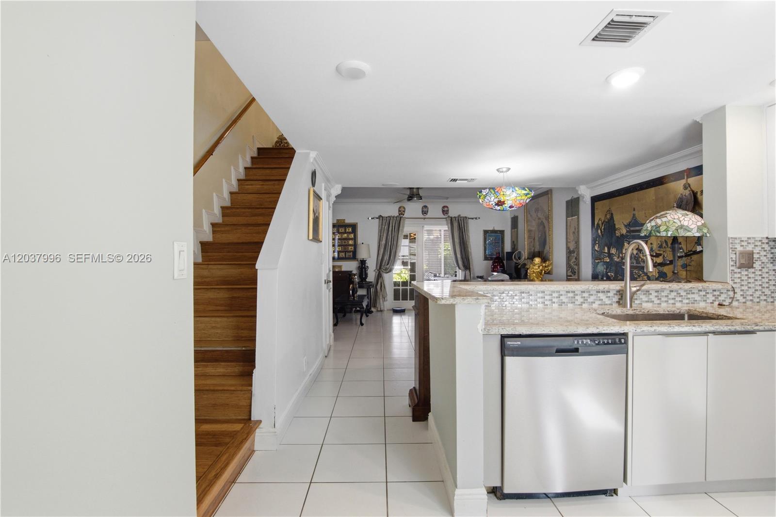 A kitchen with a stainless steel dishwasher and granite countertop overlooks a tiled living area — POMPANO BEACH, FL
