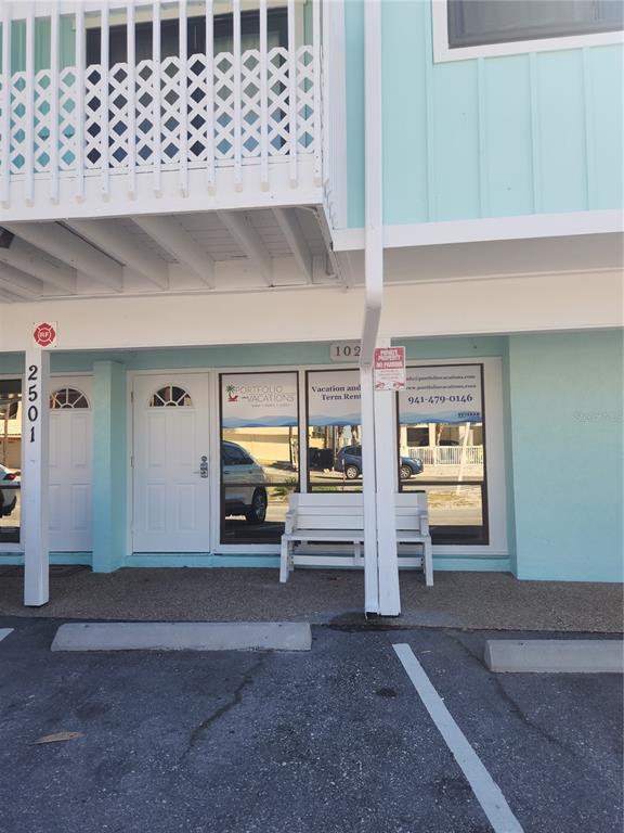 The exterior of a light blue building features a white door, windows, and a bench — 2501 GULF DRIVE N UNIT 102, BRADENTON BEACH, FL