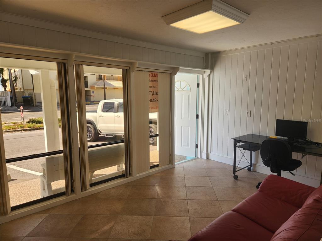 A sunroom with tile flooring, white paneled walls, a desk, and a red sofa — 2501 GULF DRIVE N UNIT 102, BRADENTON BEACH, FL