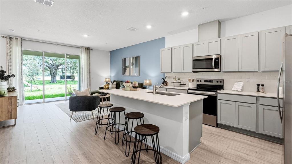 A modern kitchen with gray cabinets and a white island overlooks an open living area — 3516 CHROMA STREET, ORLANDO, FL