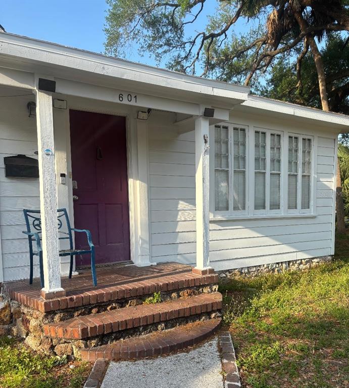 A white house exterior features a purple front door, brick steps, and a covered porch — 2601 W CLEVELAND STREET, TAMPA, FL