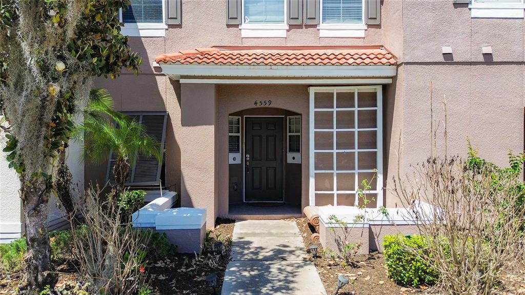 The exterior of a house features a front door, a tiled entryway roof, and landscaping — 4559 CORSA LANE, KISSIMMEE, FL
