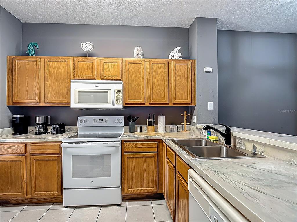 A kitchen features oak cabinets, white appliances, and marble-patterned countertops against a dark gray wall — 4559 CORSA LANE, KISSIMMEE, FL