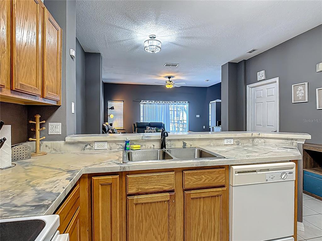 A kitchen with wood cabinets and stone countertops overlooks an open living area — 4559 CORSA LANE, KISSIMMEE, FL