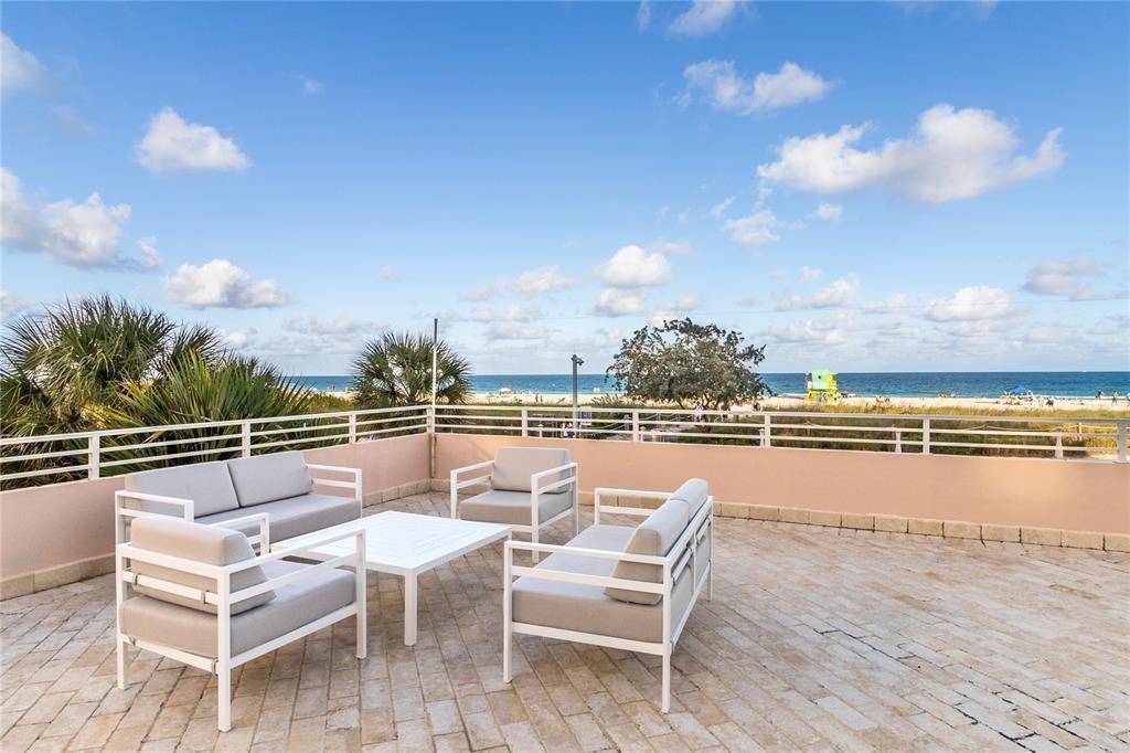 A patio with white metal furniture overlooks a sandy beach and the ocean — 345 Ocean Drive # 512, Miami Beach FL 33139, MIAMI BEACH, FL