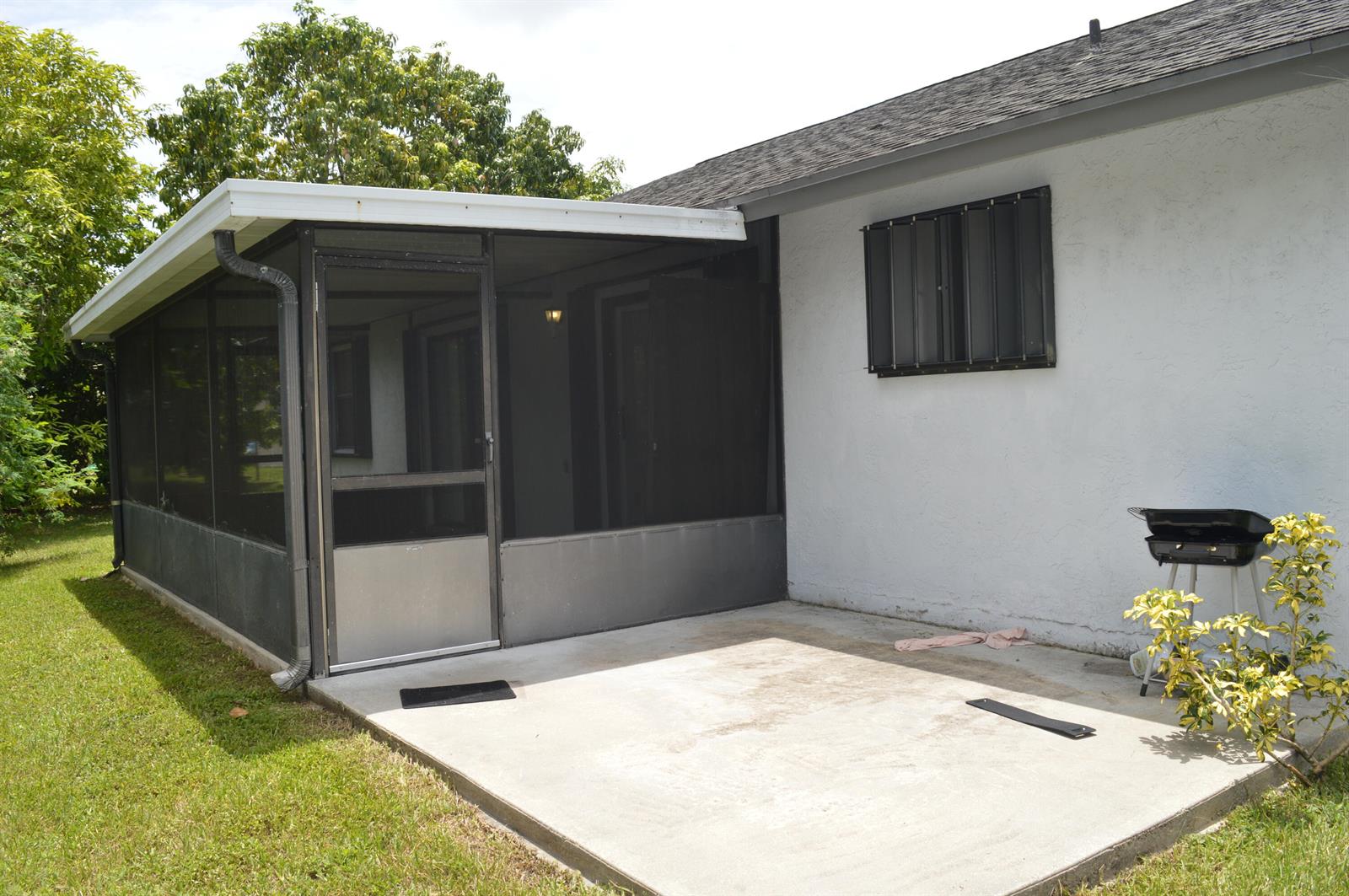 A concrete patio sits beside a screened-in porch and a white house with a grill — 9194 NW 49TH Court, Sunrise FL 33351, SUNRISE, FL