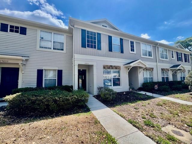 A multi-story townhouse exterior features light gray siding, dark shutters, and a concrete walkway — 15655 STABLE RUN DRIVE, SPRING HILL, FL