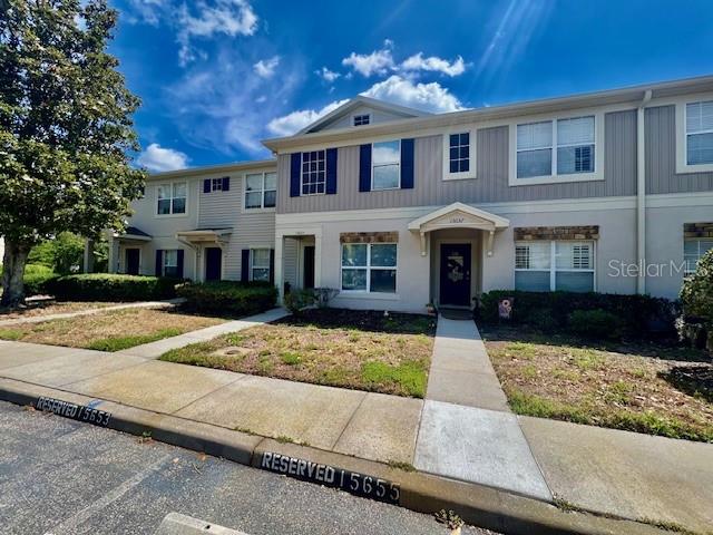 A two-story townhouse with light-colored siding and a covered entryway under a blue sky — 15655 STABLE RUN DRIVE, SPRING HILL, FL