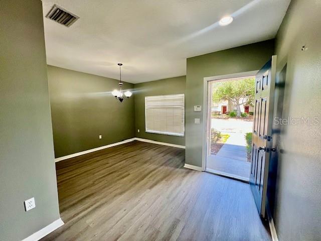 An empty room with olive green walls, wood-look flooring, a chandelier, and an open door — 15655 STABLE RUN DRIVE, SPRING HILL, FL