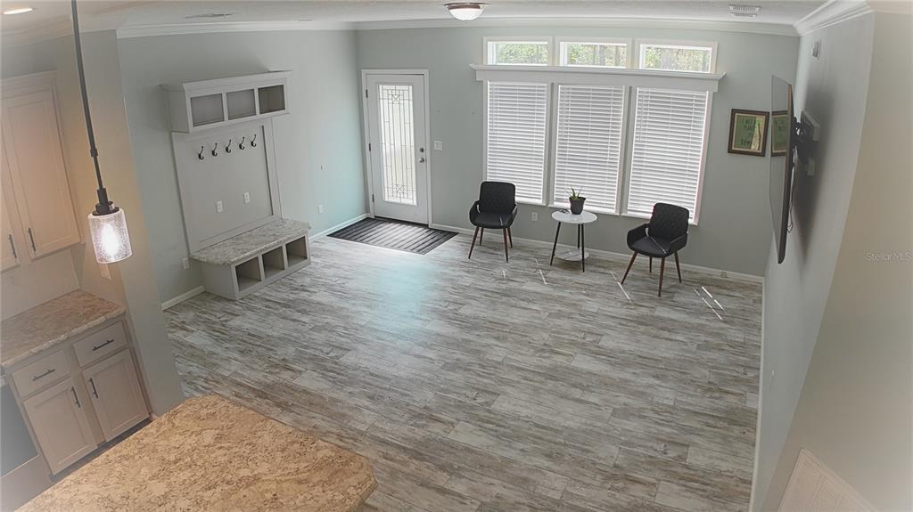 An open-concept living area features wood-look tile flooring, a built-in mudroom bench, and large windows — 10750 NW 190TH STREET, MICANOPY, FL