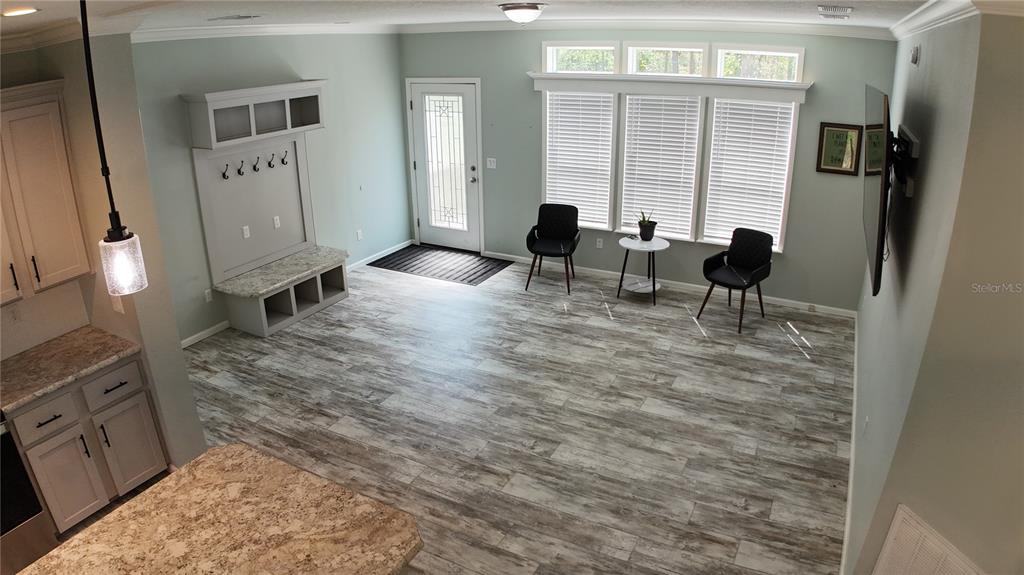 An open-concept living area features wood-look tile flooring, a built-in mudroom bench, and large windows — 10750 NW 190TH STREET, MICANOPY, FL