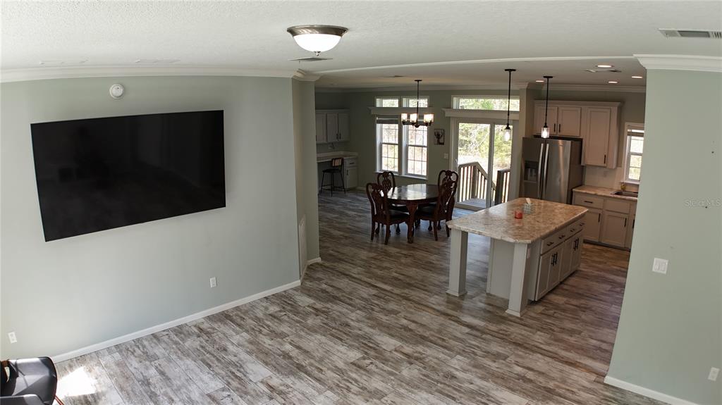 An open-concept living room and kitchen featuring light wood-look flooring and a large island — 10750 NW 190TH STREET, MICANOPY, FL