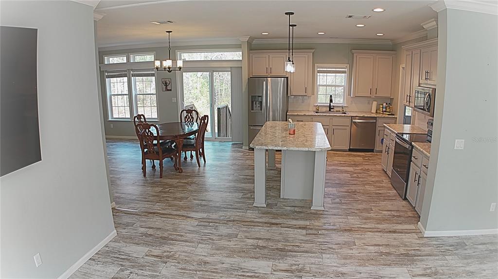 A kitchen with an island and dining area features light-colored cabinets and wood-look tile flooring — 10750 NW 190TH STREET, MICANOPY, FL